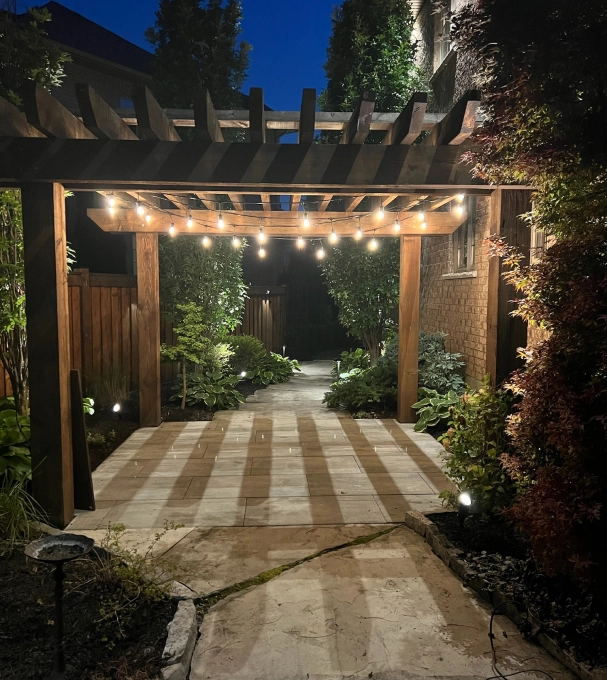 Evening garden walkway lit with warm low voltage summer outdoor lighting under a pergola in a GTA home, showcasing how landscape lighting transforms patios and paths in Mississauga, Vaughan, and surrounding areas.